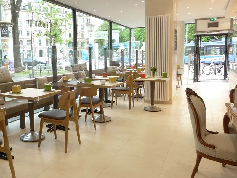 Tische und Stuehle stehen in einem modernen, hellen Cafe mit grossen Fenstern und Stadtblick. Text: Backhaus Kreutzkamm.