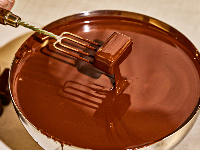 Gabel taucht Praline in fluessige Schokolade, eine Schuessel mit glatter Oberflaeche.