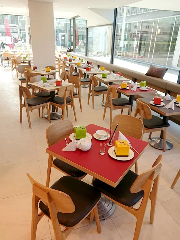 Tische im Cafe, gedeckt mit bunten Serviettenhaltern und Geschirr, in hellem, modernem Raum.