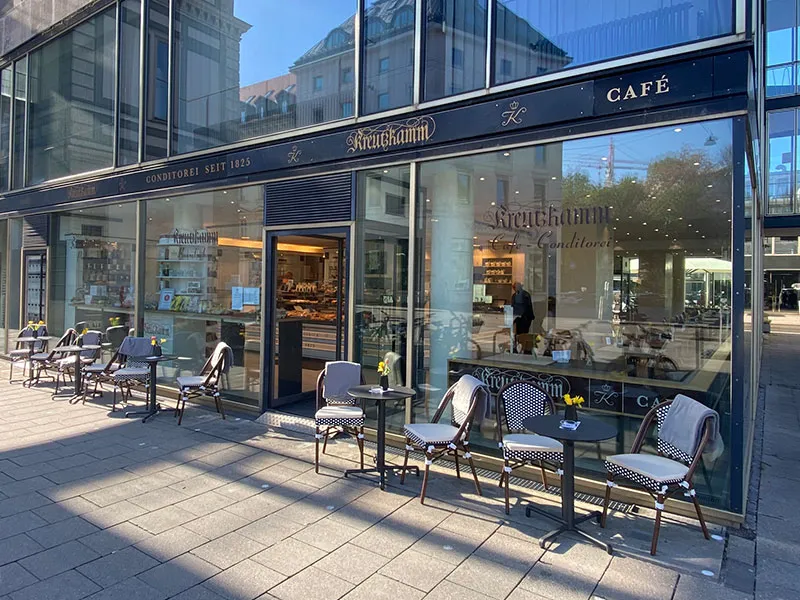 Cafe mit aussen Sitzplaetzen vor glasfrontigem Gebaeude, Beschriftung 'Kreutzkamm Konditorei seit 1825'.